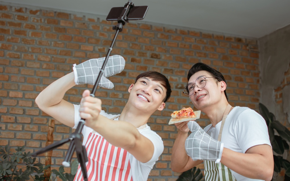 Two asian handsome male bloggers online streaming video clip of cooking in kitchen at home. Technology, Social Media, LGBT and Lifestyle Concept.