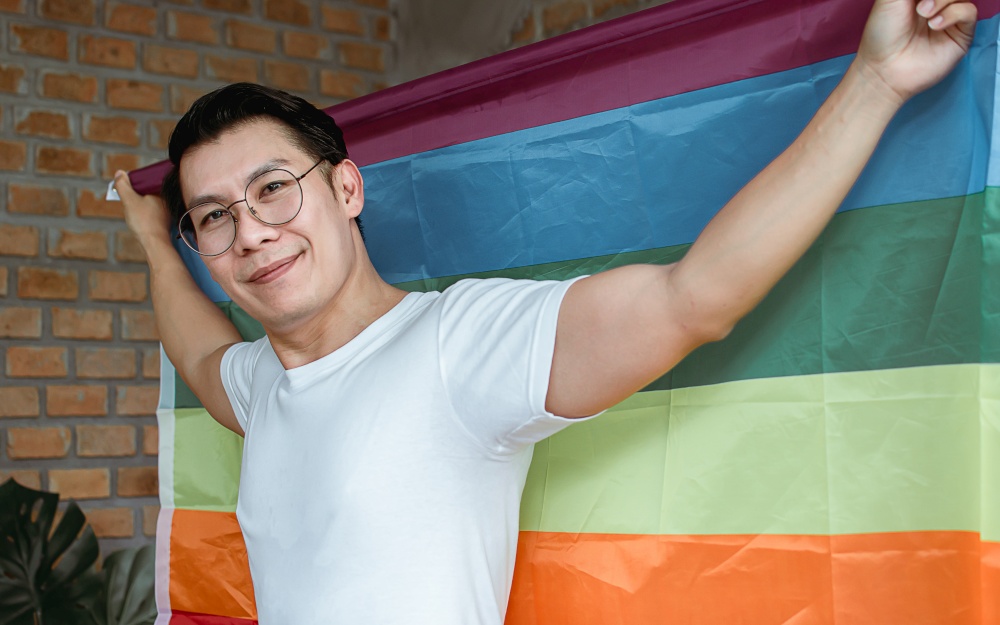 Asian handsome man wearing white shirt and holding rainbow flag. Lifestyle and LGBT Concept.