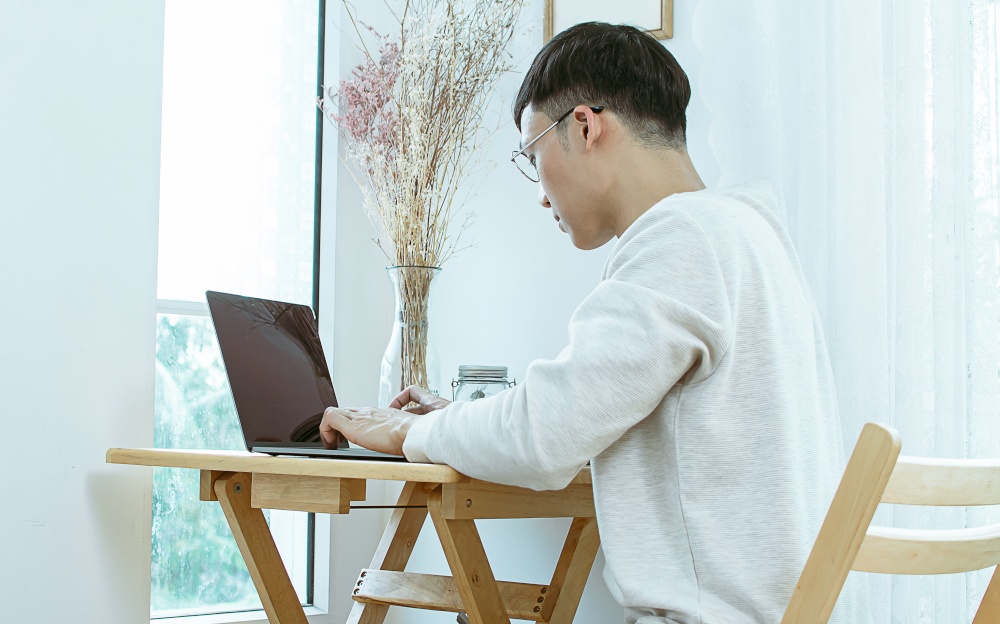 A man wearing casual shirt, using laptop for work or online shopping while staying in bedroom at home. Lifestyle and Technology Concept.