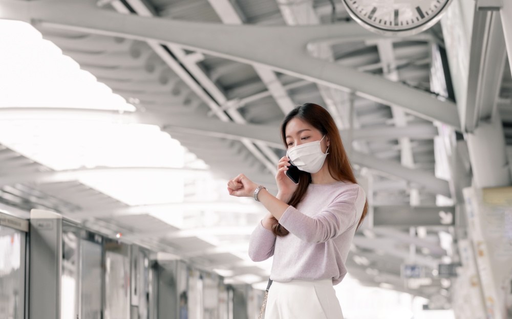 Asian woman wearing face mask and dressing casual business, waiting for a train while standing on railway station and going to work. New Normal, Socian Distancing and Transportation Concept.