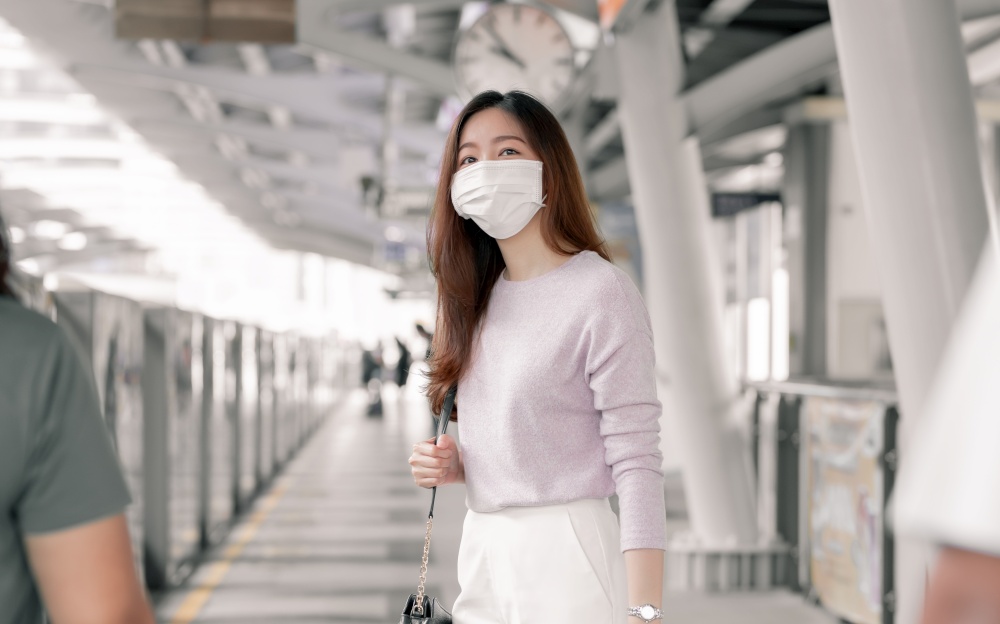 Asian woman wearing face mask and dressing casual business, waiting for a train while standing on railway station and going to work. New Normal, Socian Distancing and Transportation Concept.
