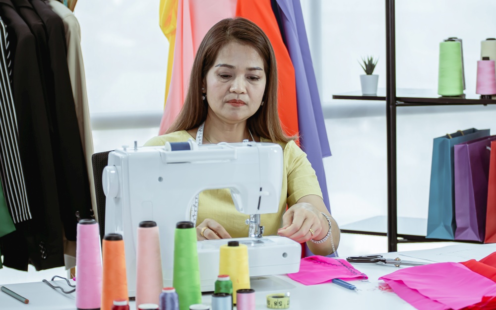A senior fashion designer is using sewing machine for making dress