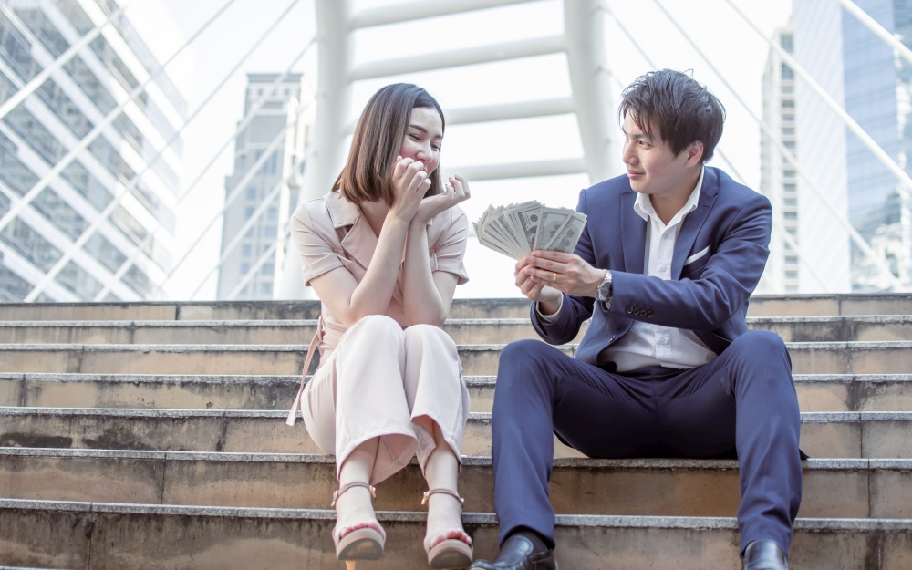 Asian man giving a lot of money to his girlfriend. Business Concept.