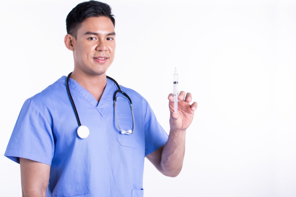 Asian young male doctor wearing uniform and using syringe for vaccing injection while standing on white background with copy space. Medical and Virus protection Concept.