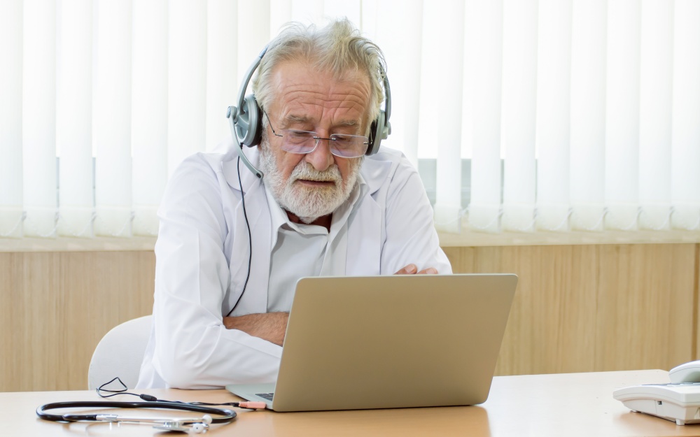 Caucasian senior doctor wearing headset and making online video conference to giving advice to patient with copy space. Medical and Technology concept.