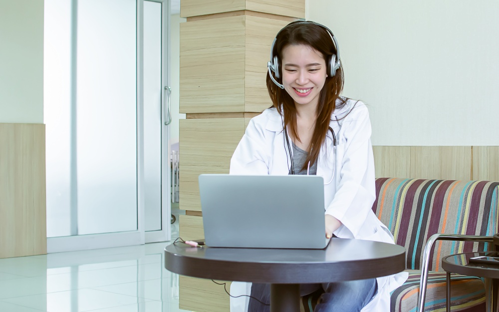 Asian beautiful doctor using laptop to advice about health information to a patient by online video conference. Social Distancing and New Normal Concept