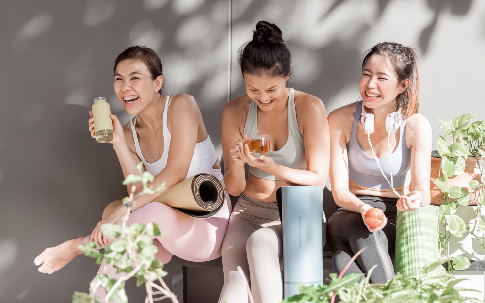 Asian women wearing sport bra, talking and laughing together after doing exercise in yoga class at gym. Sport, Friendship and Healthy Concept.