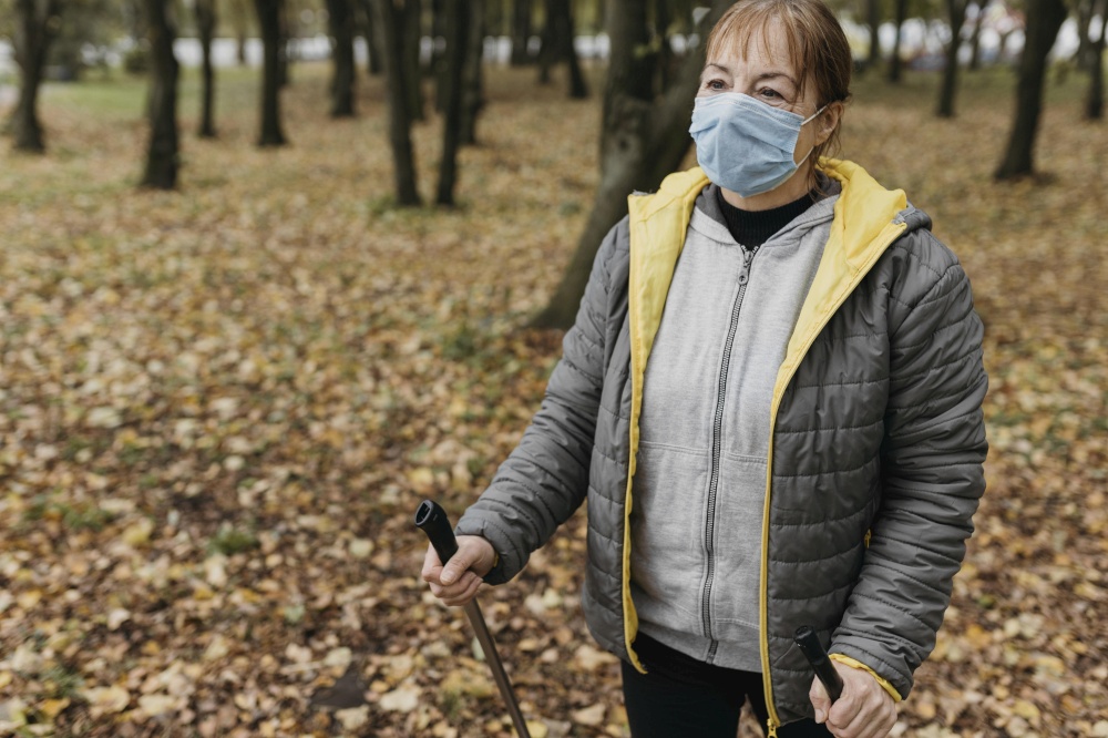 senior woman with medical mask trekking sticks outside