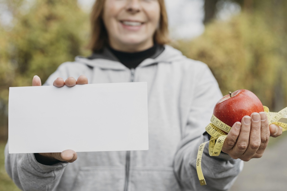 smiley elderly woman holding apple paper outdoors while working out