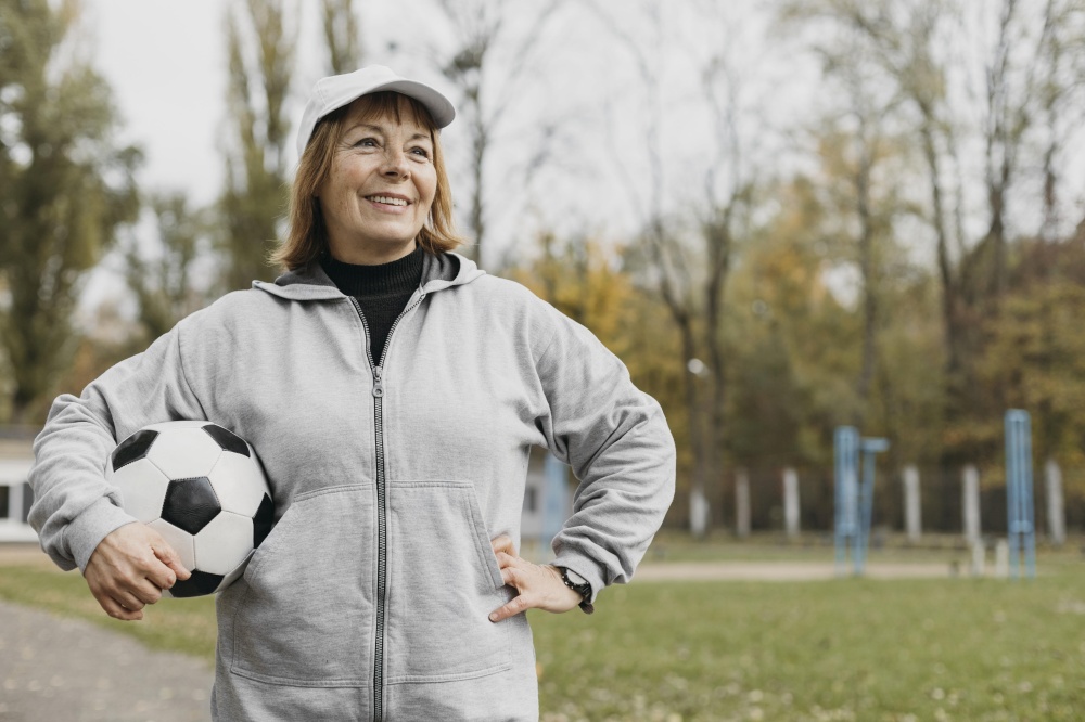 smiley elderly woman holding football outdoors while working out