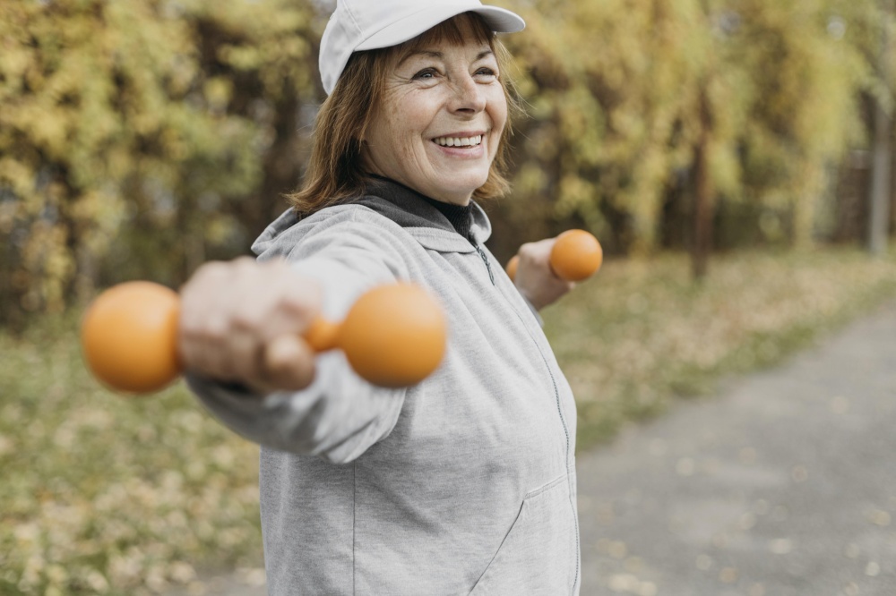 smiley elderly woman working out with weights outdoors