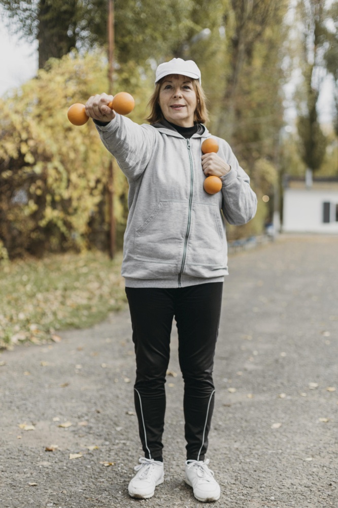 smiley elderly woman working out with weights outside