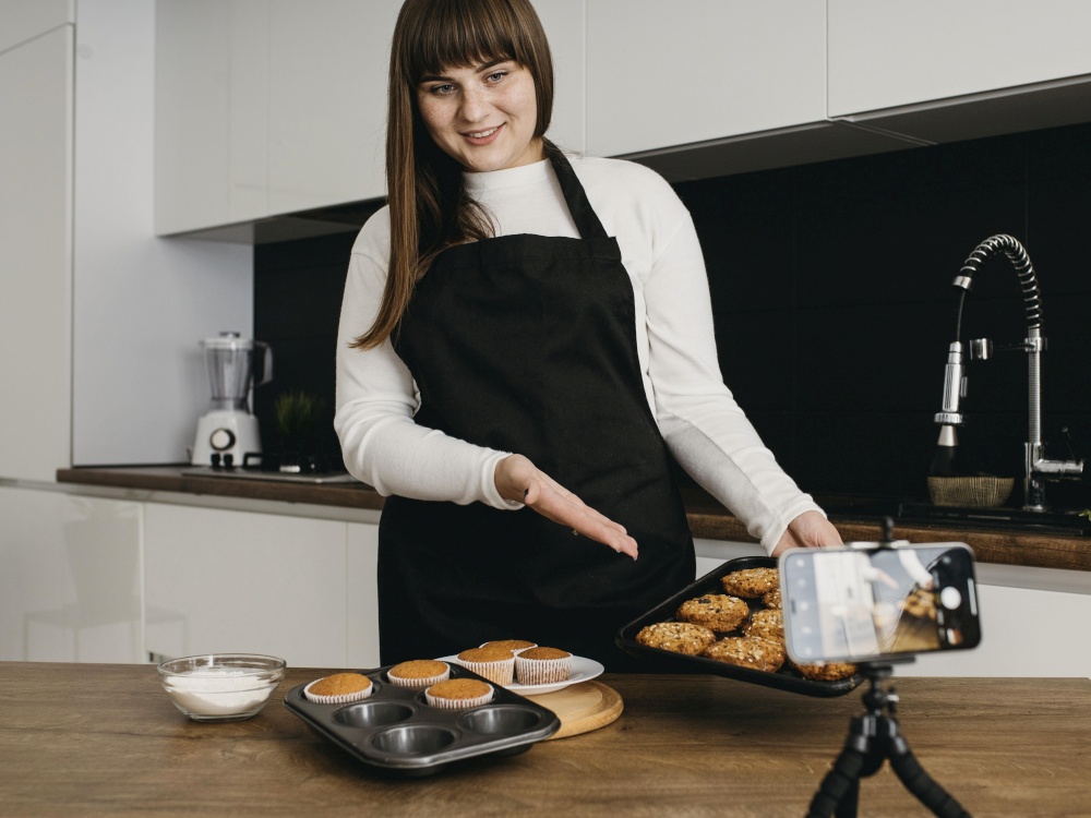 smiley female blogger recording herself while preparing muffins