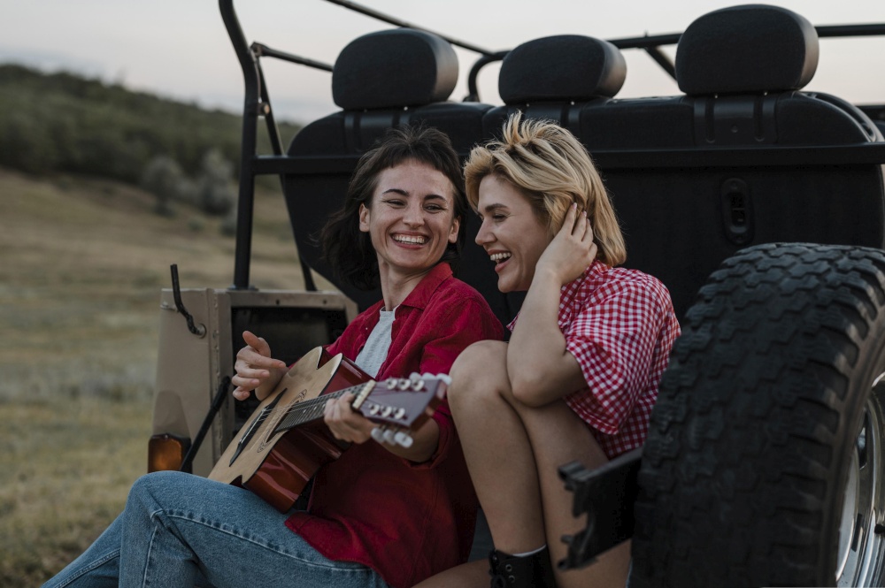 smiley female friends playing guitar while traveling by car