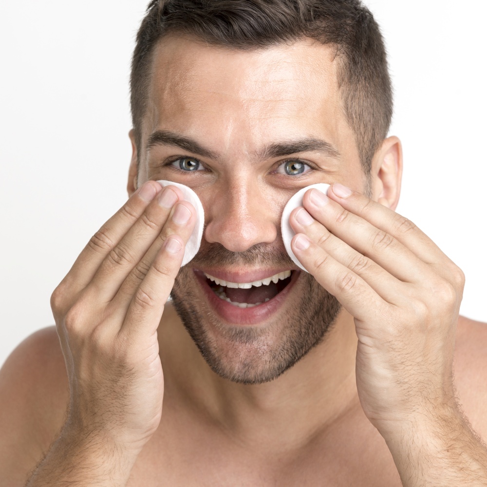close up man cleaning his face with cotton pad smiling