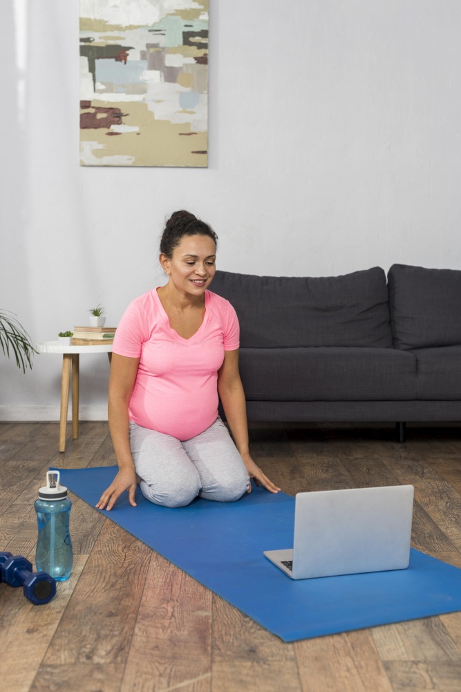 smiley pregnant woman home exercising with laptop