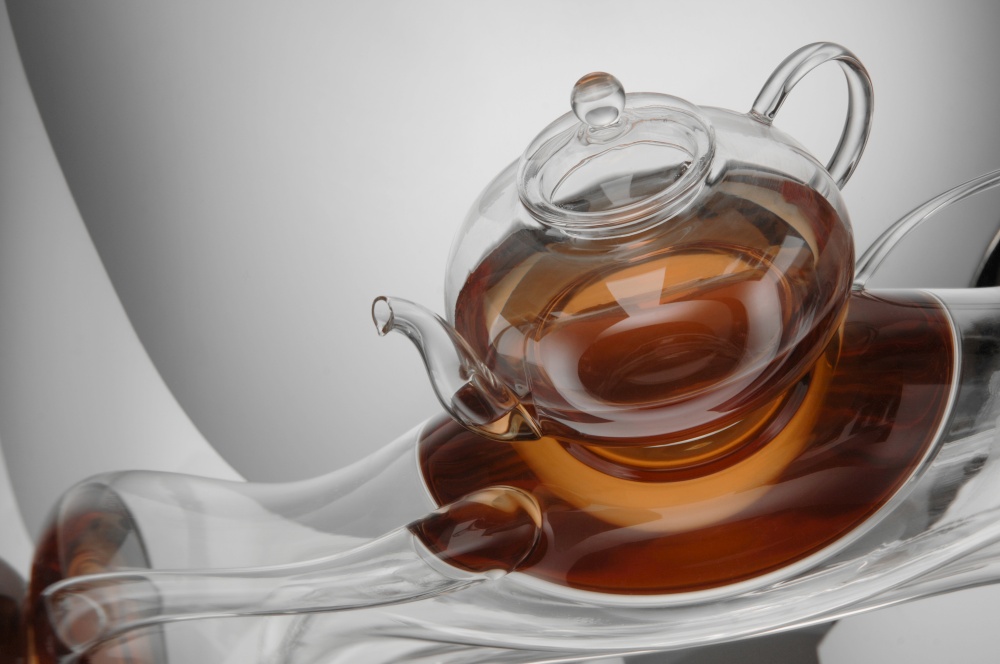 transparent teapot with tea on the reflective surface on a light gray background. distorted reflection. kitchen transparent kettle