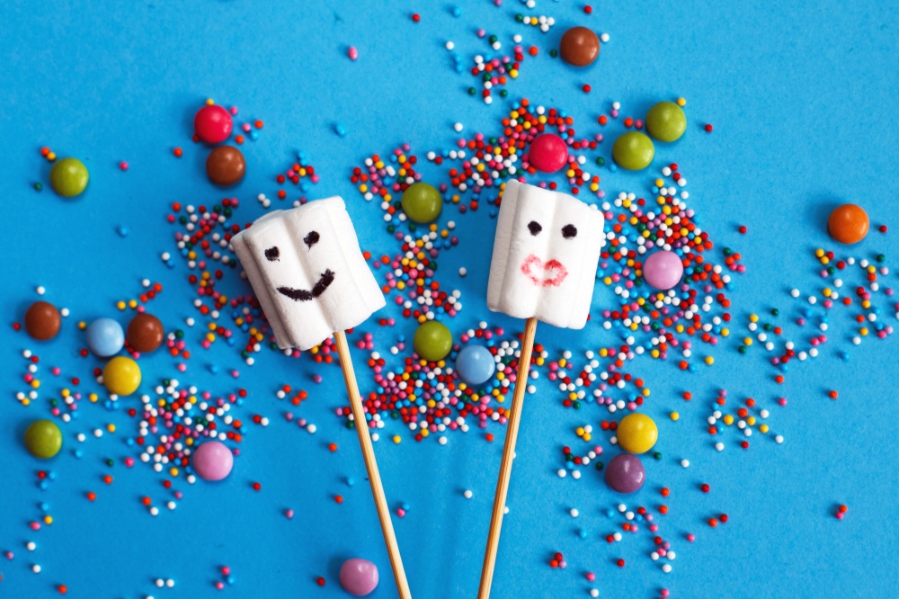 marshmallows composition on wooden skewers with color sweets on blue background. Flat lay, holiday concept. sweets in the form of people. marshmallows on wooden skewers with color sweets on blue background. holiday concept. sweets in the form of people