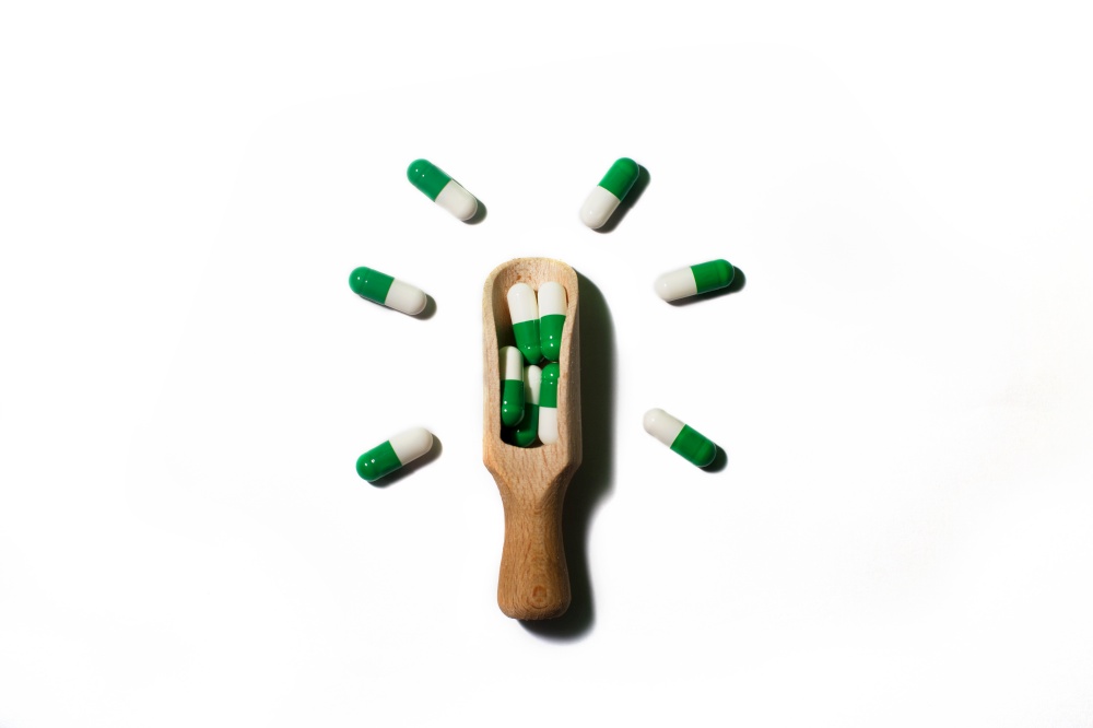 medicine green pills on white background on wooden spoon in the form of a light bulb . Copy space for text.. medicine green pills on white background on a wooden spoon in the form of a light bulb . Copy space for text.