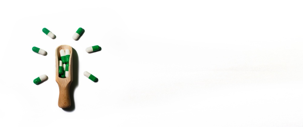 medicine green pills on white background on wooden spoon in the form of a light bulb . Copy space for text. banner. medicine green pills on white background on a wooden spoon in the form of a light bulb . Copy space for text. banner