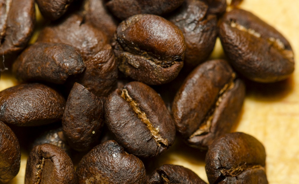 macro shot of a bunch of roasted coffee beans on a wooden table.