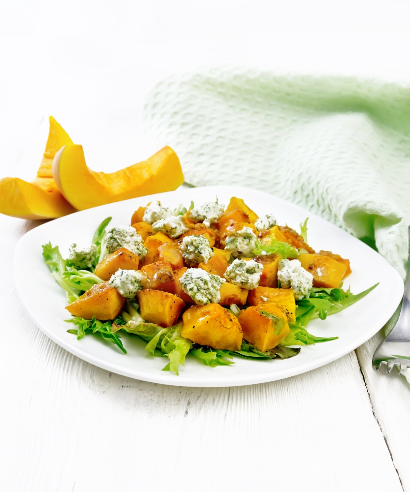 Salad of baked pumpkin, arugula with balls of salt cheese, seasoned with honey, grainy mustard, garlic and vegetable oil in a plate, napkin and fork on wooden board background