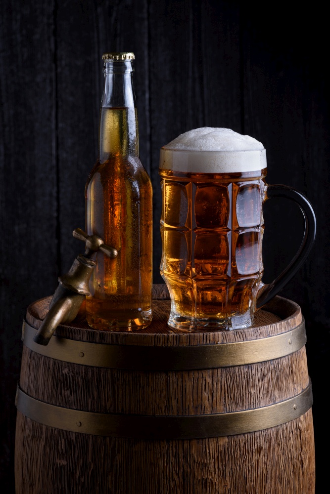 Beer glass and bottle on vintage wooden barrel with old tap, dark background