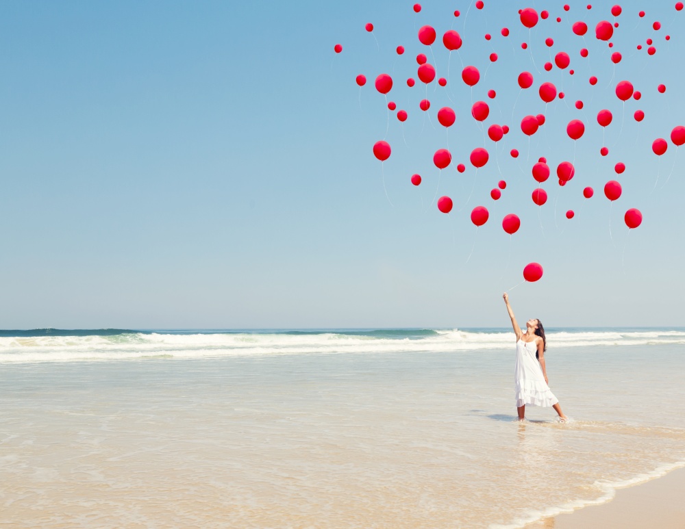 Beautiful girl in the beach dropping red ballons in the sky