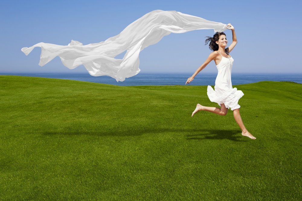 Beautiful woman running and jumping on a green meadow with a white tisue