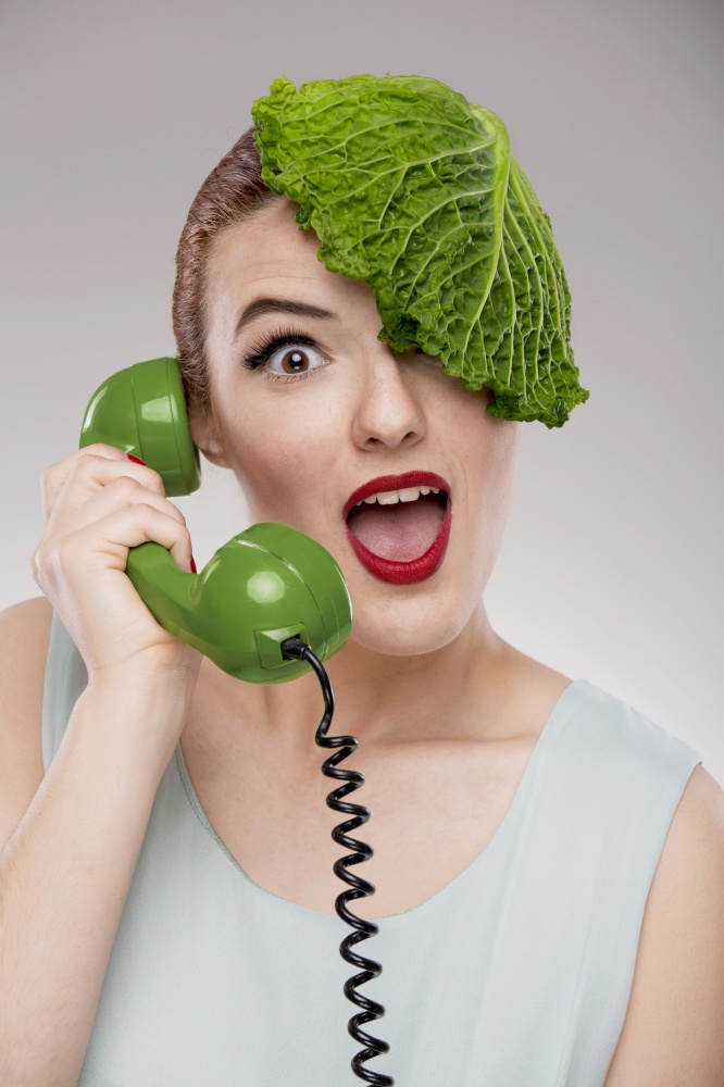 Portrait of a woman illustrating a vegan concept with a cabbage on the head and making a ecological green call