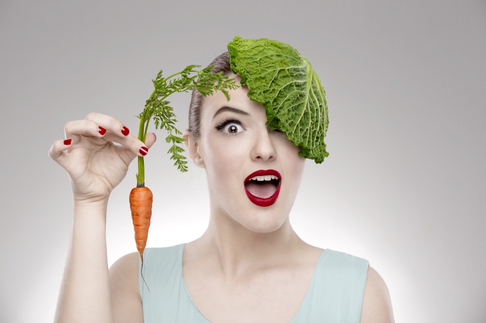 Portrait of a woman illustrating a vegan concept holding a carrots and with a cabbage on the head. Vegan Girl