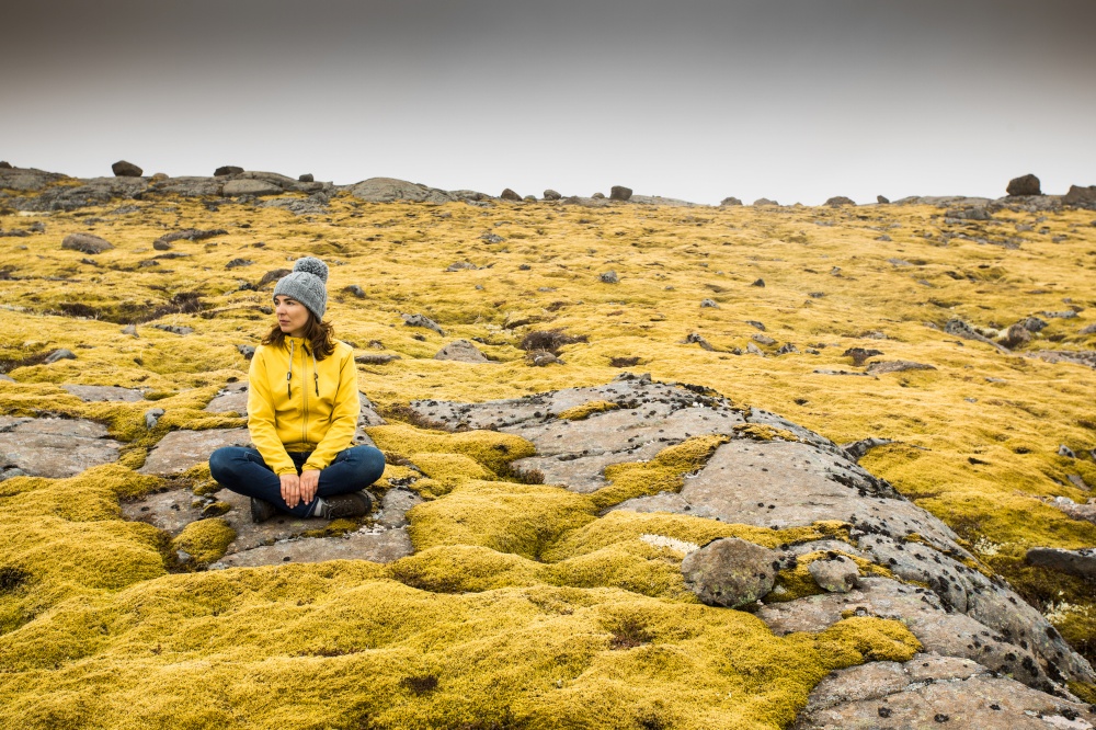 Beautiful young woman sitting on a rock and surrounded by Icelandic moss