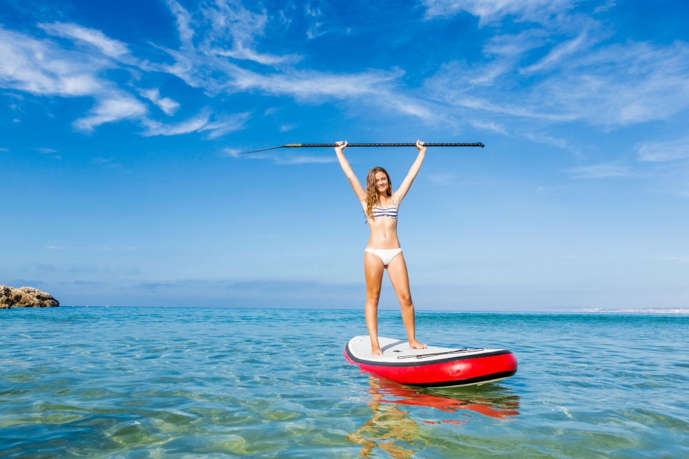 A beautiful and happy woman with arms up and learning paddle-surf