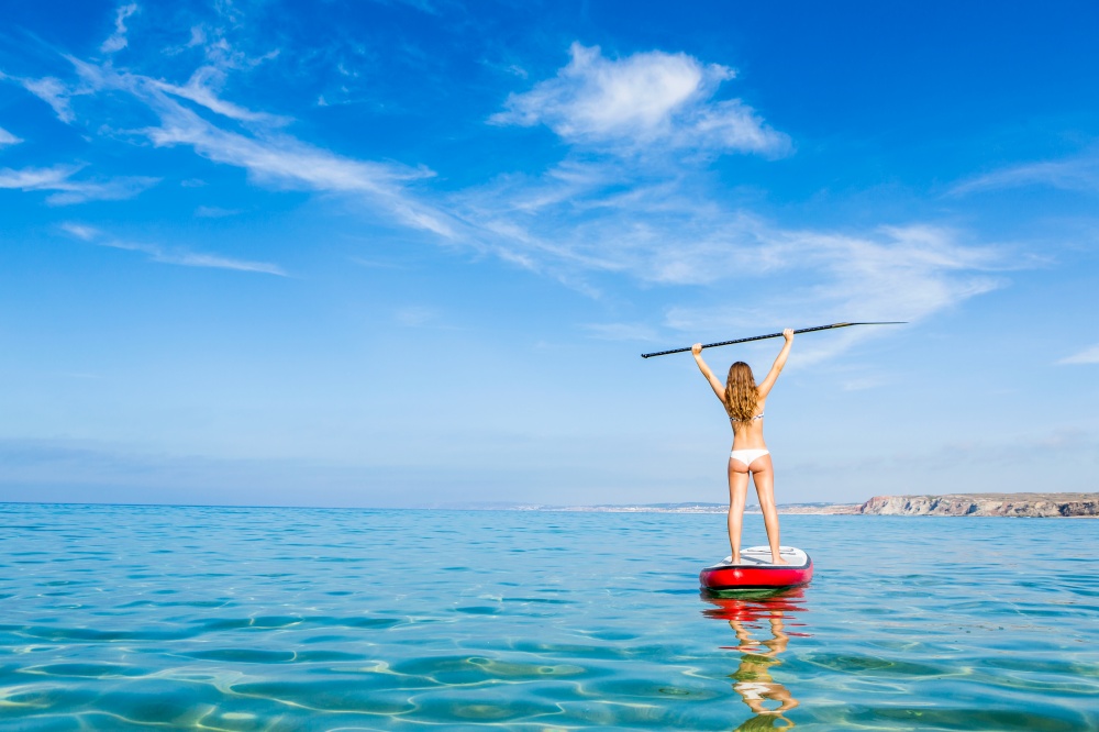 A beautiful and happy woman with arms up and learning paddle-surf