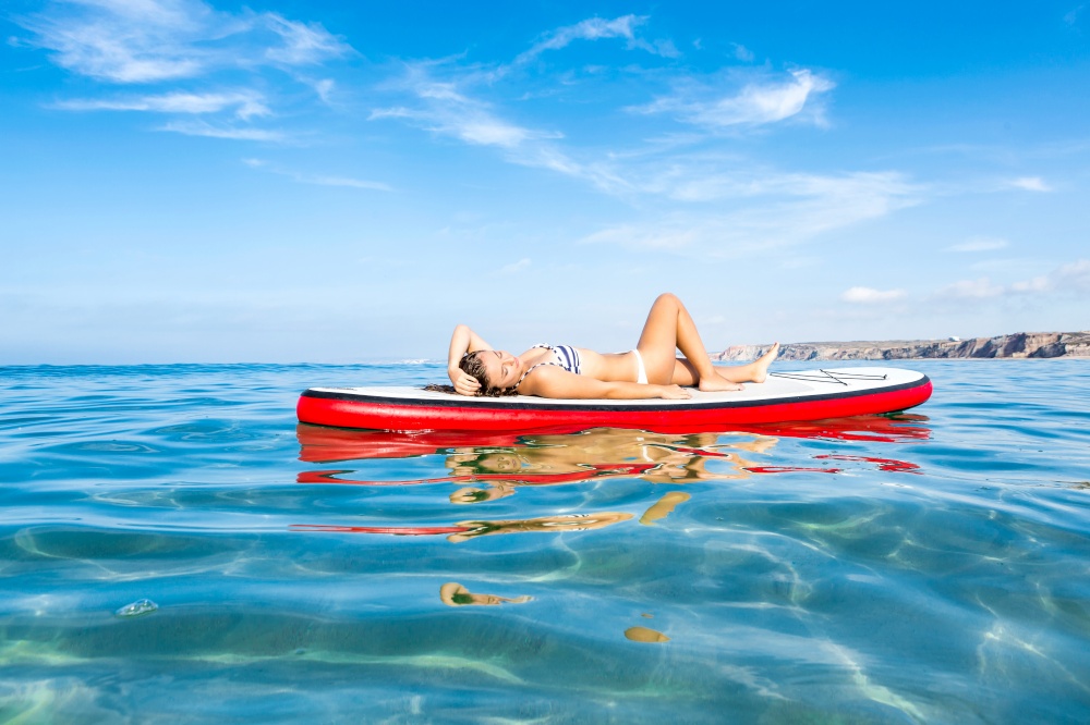 A beautiful woman sitting over a paddle surfboard and relaxing on a beautiful sunny day
