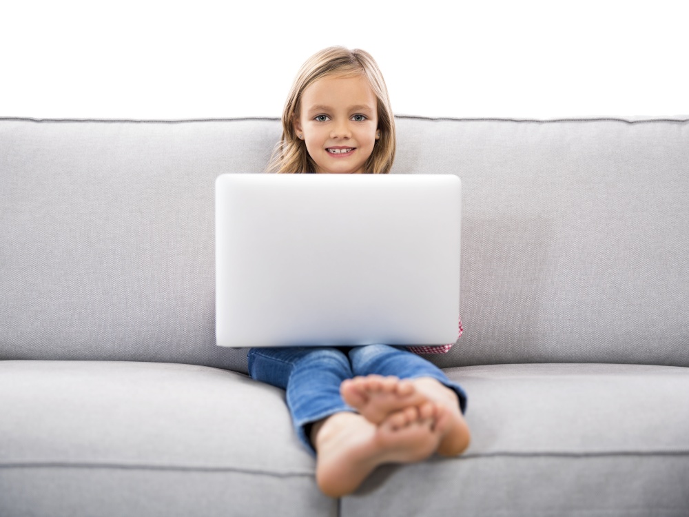 Happy little girl sitting on a couch and working a laptop