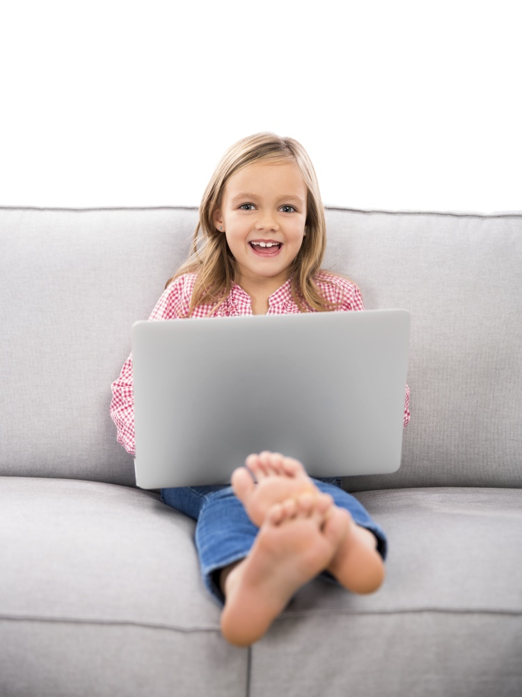 Happy little girl sitting on a couch and working a laptop