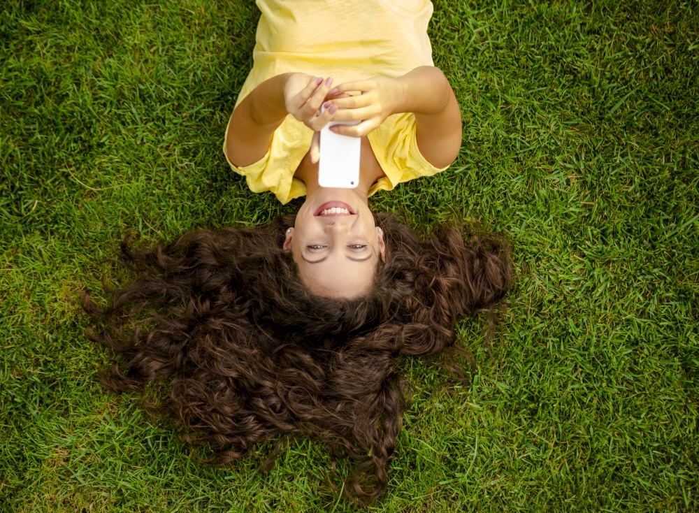 Smiling young woman lying on the grass and making a selfie