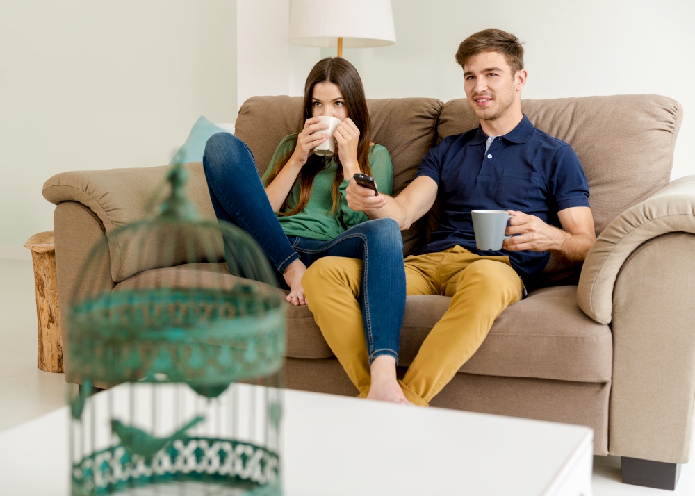 Young couple on the sofa drinking coffee while watching tv