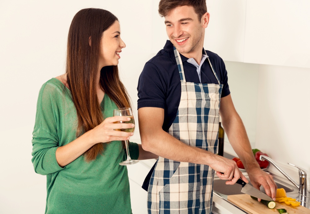Young couple on the kitchen cooking and the girl enjoy a glass of wine