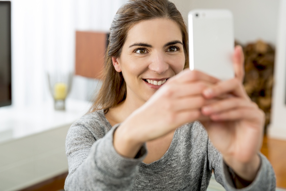 Beautiful woman taking a photo of herself with her smartphone at home