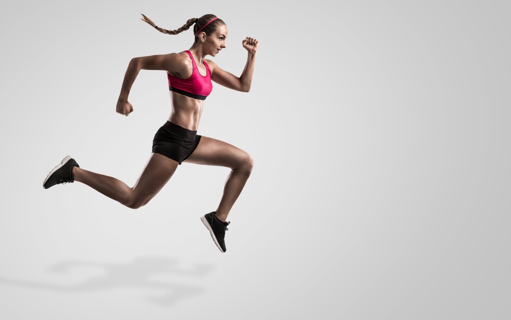 Shot of a sporty young woman runing and jumping against a gray background