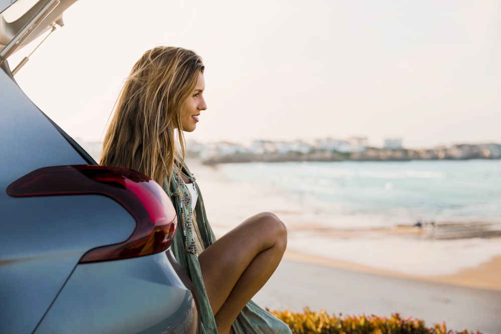 Beautiful woman sitting in the trunk of a car and looking to the sea