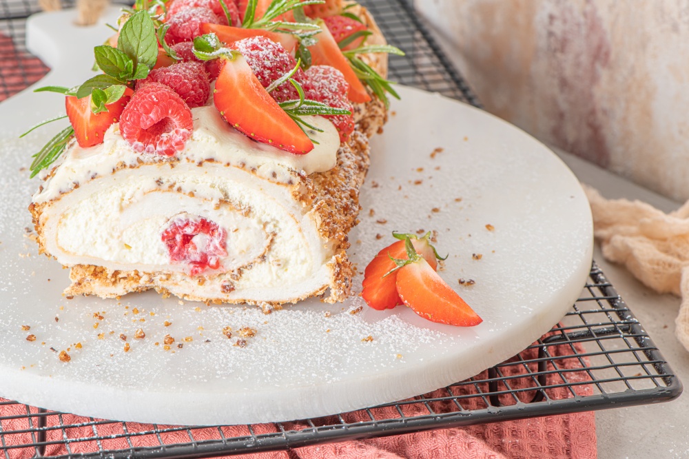 Meringue roll with a gentle airy cream, crunchy peanut, mint, rosemary and filling with raspberries and strawberries. Pavlova summer sweet dessert.