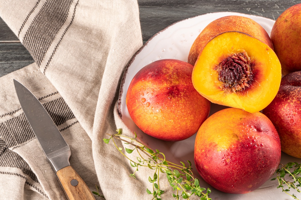 Ripe peaches with thyme leaves in a plate on a wooden board on a background