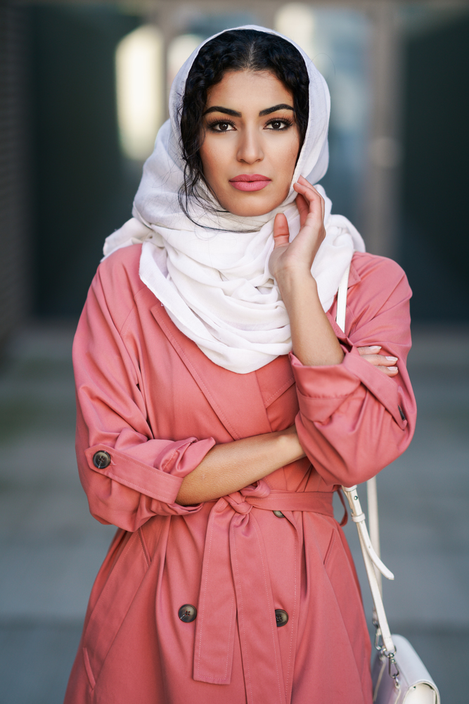 Young Muslim woman wearing hijab headscarf walking in the city center. Arab female in urban background. Young Arab woman wearing hijab headscarf walking in the city center.