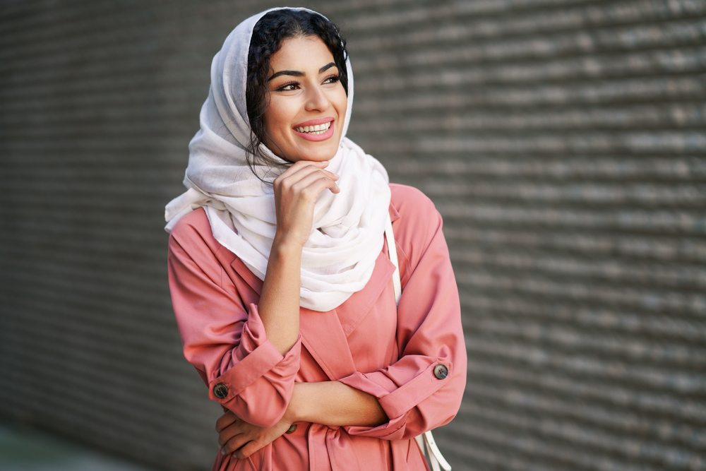 Happy Arab woman wearing hijab headscarf walking in the city center. Muslim female in urban background. Young Muslim woman wearing hijab headscarf walking in the city center.