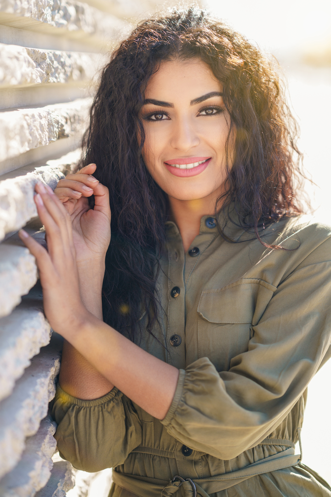 Smiling Arab Woman with curly hair in urban background. Young Arab Woman with curly hair outdoors