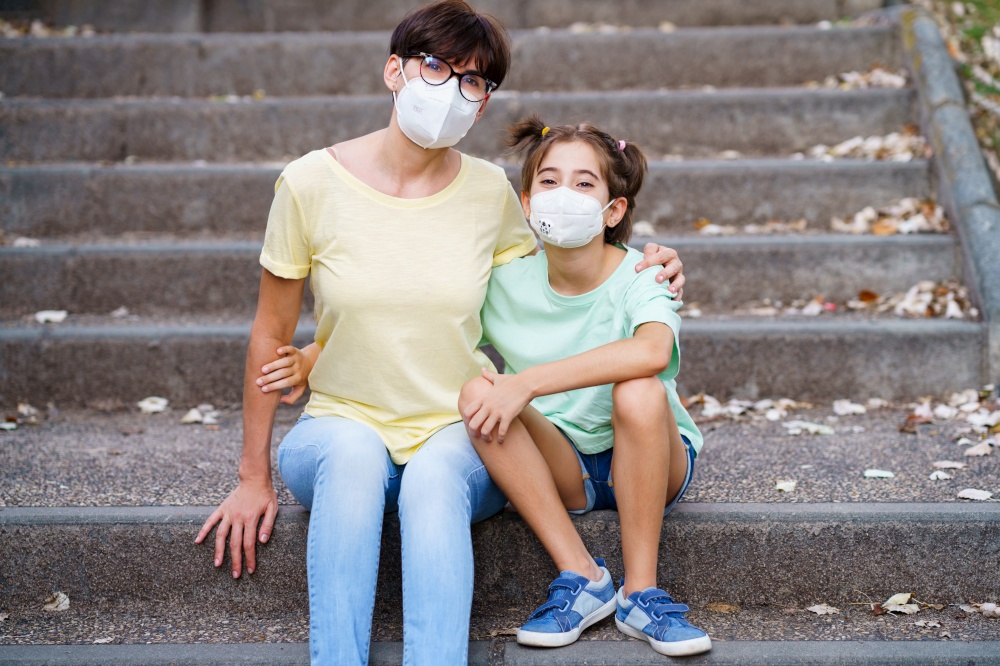 Middle-aged mother and daughter sit on the street wearing masks because of the Covid-19 pandemic. Middle-aged mother and daughter sit on the street wearing masks