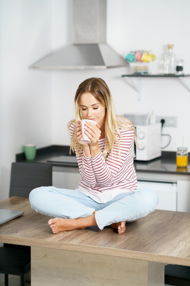 Young caucasian woman smelling a cup of coffee at home.. Young woman holding a cup of coffee at home.